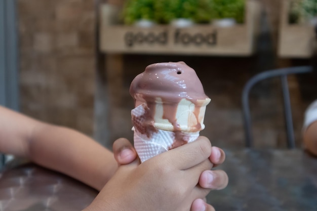 Een hand van een jong kind met een druppelende chocolade ijsje in het café