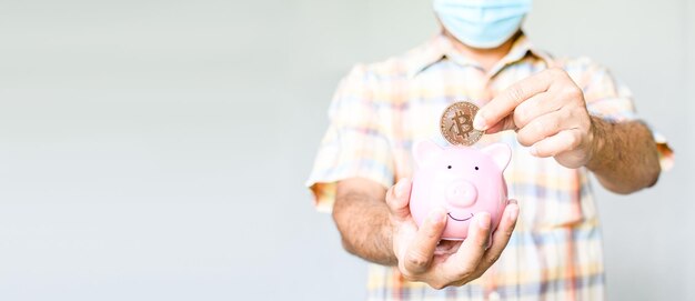 Een hand van een man die een bitcoin munt vasthoudt om een roze varken spaarpot te laten vallen het concept voor het besparen van geld