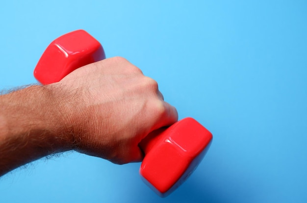 Een hand van een man houdt een rode plastic dumbbell vast op een blauwe achtergrond