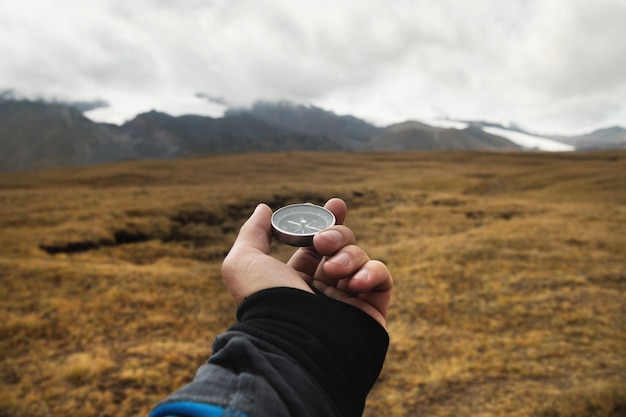 Foto een hand van een reiziger houdt een magnetisch kompas vast tegen de achtergrond van een berglandschap