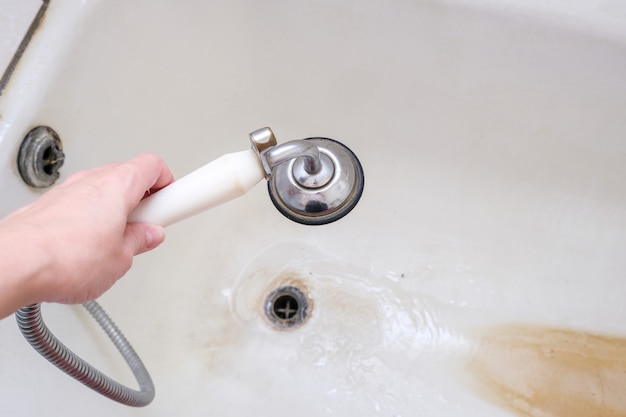 Een handdouche met stromend water tegen roestige badkuip met kalkaanslag