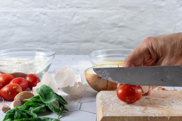 Een handsnijdende tomaat tussen ingrediënten en keukengerei