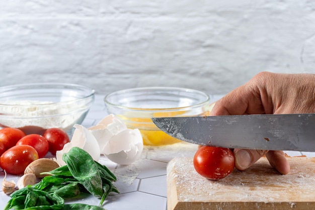 Een handsnijdende tomaat tussen ingrediënten en keukengerei