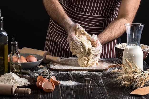 Een handvol bloem met ei op een rustieke keuken. Kneed het deeg tegen de achtergrond van mannenhanden. Ingrediënten voor het koken van meelproducten of deegbrood, muffins, taart, pizzadeeg. Ruimte kopiëren