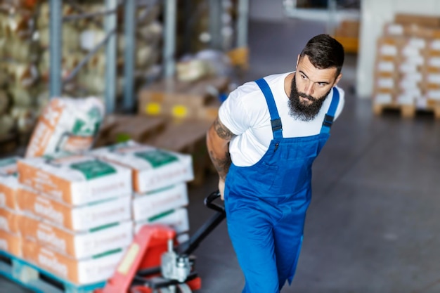 Foto een hardwerkende bebaarde magazijnmedewerker trekt een vorkheftruck vol vracht en verplaatst deze