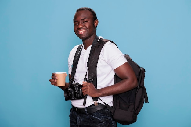 Een hartelijk lachende fotografie-enthousiasteling die een reisrugzak en een professionele camera draagt, klaar voor een vakantiereis. Zelfverzekerde toerist met DSLR-apparaat terwijl hij opgewonden is voor een stedentrip.