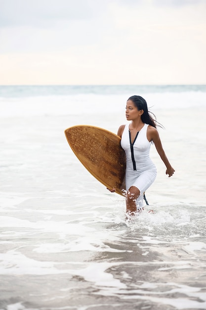 Een heel mooi gebruind surfermeisje komt bij bewolkt weer met een surfplank uit de zee