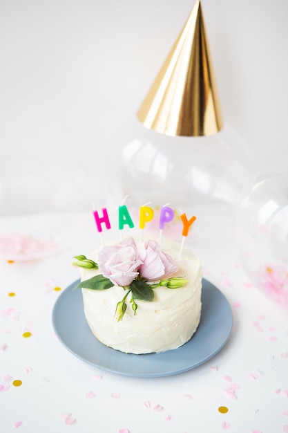 Een heel mooie kleine witte cake versierd met verse eustoma bloemen tegen de achtergrond van snoep en de inscriptie gelukkige verjaardag ballonnen hoeden vakantie concept