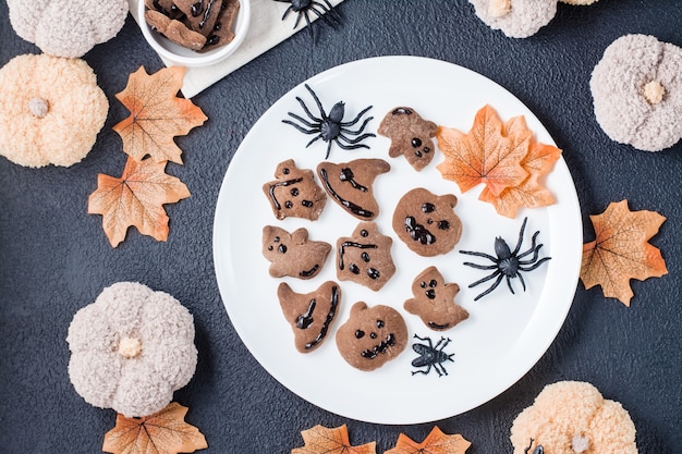 Een heerlijke Halloween-traktatie - peperkoekkoekjes met chocoladesuikerglazuur in kommen op een tafel met pompoenen, bladeren en spinnen. Traditionele viering. Bovenaanzicht