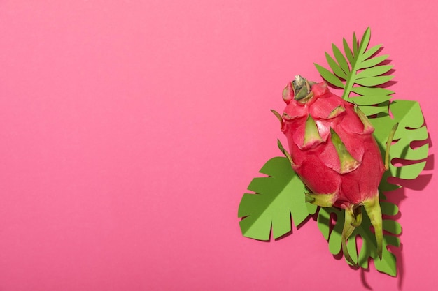 Foto eén hele drakenvrucht en papieren tropische bladeren op roze achtergrond ruimte voor tekst