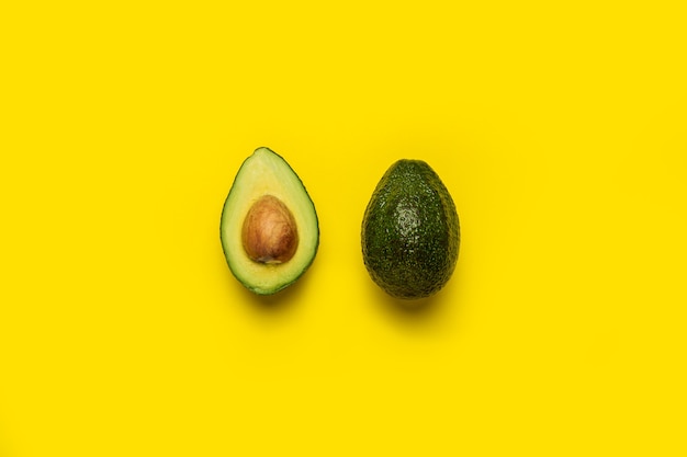 Een hele en een halve avocado op een heldergeel