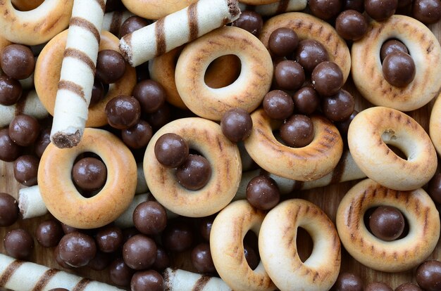 Een heleboel knapperige zoete buisjes, chocoladesmeltkogels en gele bagels liggen op een houten oppervlak. sluit omhoog mening