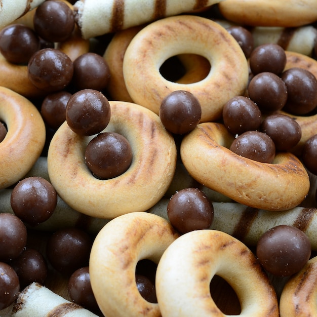 Een heleboel knapperige zoete buisjes, chocoladesmeltkogels en gele bagels liggen op een houten oppervlak. sluit omhoog mening