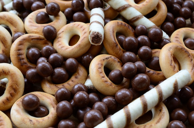 Een heleboel knapperige zoete buisjes, chocoladesmeltkogels en gele bagels liggen op een houten oppervlak