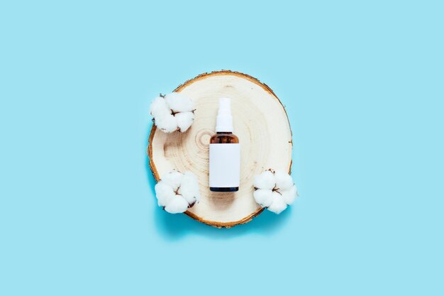 Een herbruikbare glazen fles met geen afval, omringd door katoenbloemen op een houten dienblad