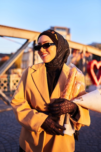 Een hijab-vrouw met een stijlvolle zonnebril en een elegante Franse outfit die bij zonsondergang door de stad loopt