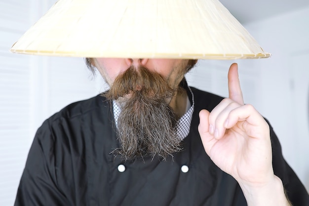 Een hilarische parodie op een Aziatische man met Vietnamese hoed en baard. Portret. Aziatische caféchef.