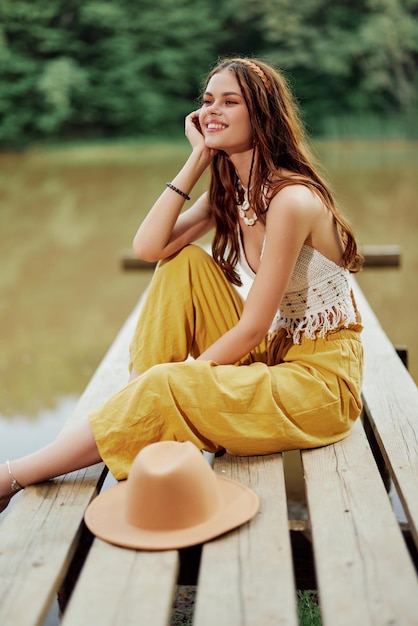 Een hippievrouw zit op een brug bij een meer op een natuurreis en glimlacht vrolijk in ecokleding