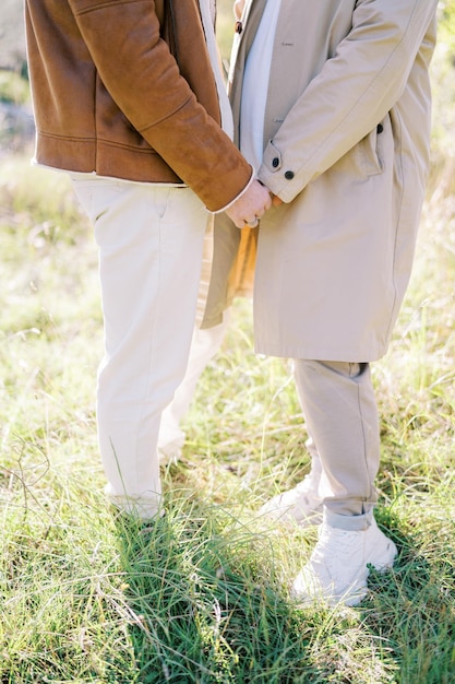 Een homoseksueel koppel staat hand in hand in een zonnige open plek tegenover elkaar, gezichtsloos geknipt.