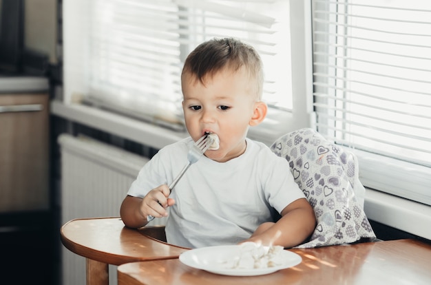 Een hongerig kind eet knoedels in de keuken, zittend in een stoel in een wit t-shirt