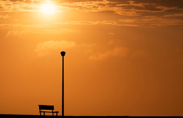 Een houten bank en straatlantaarn met een achtergrondmening van een rode zonsondergang op zonsondergang en een felle zon.