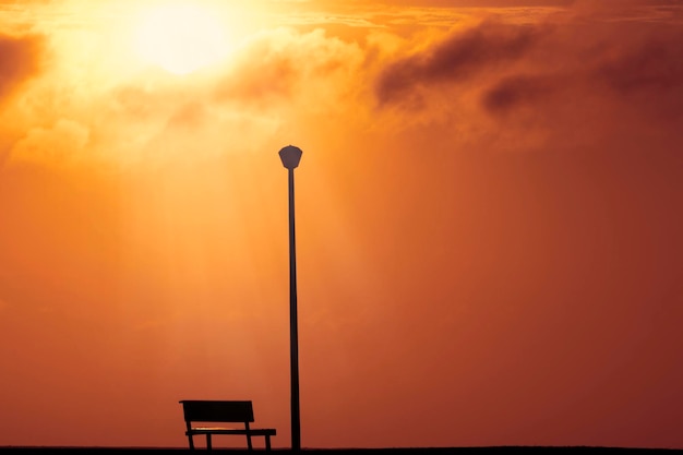 Een houten bank en straatlantaarn met een achtergrondmening van een rode zonsondergang op zonsondergang en een felle zon