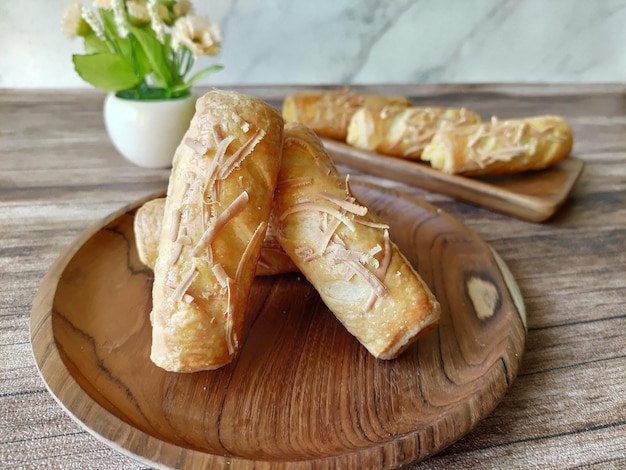 Een houten dienblad met brood erop en een vaas met bloemen op de achtergrond.