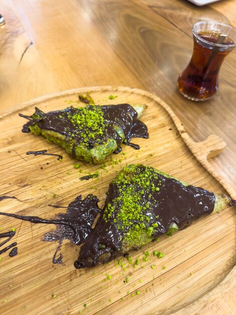 Een houten dienblad met daarop een chocoladedessert met op de achtergrond een fles thee.