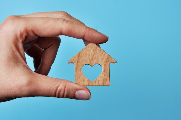 Een houten huis in de handen van een man. Een symbool van bescherming en zorg voor huis en gezin