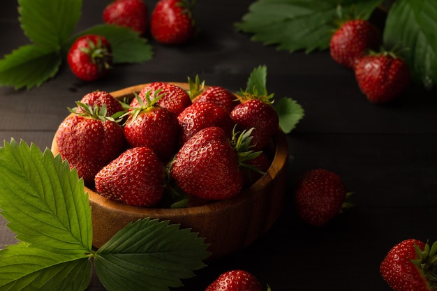 Een houten kom verse rode rijpe aardbeien op een zwarte houten ondergrond