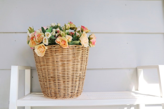 Een houten mandpot van boeket roze en oranje bloemen op de houten lijst met witte muur.