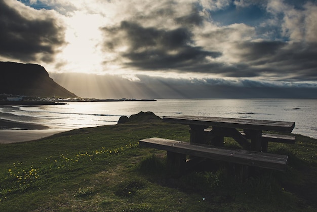 Een houten picknicktafel met prachtig uitzicht op de oceaan met zon die door de wolken schijnt in IJsland Plaats voor rustreisconcept