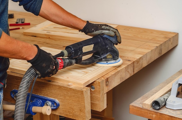 Een houten plank schuren met een elektrische handschuurmachine