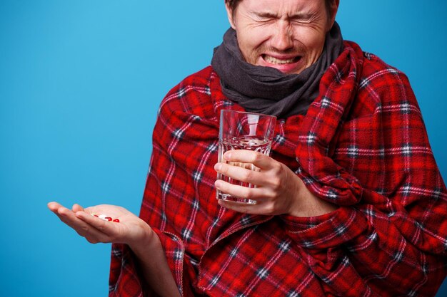 Een in een deken gewikkelde zieke man met tabletten en mok in zijn handen