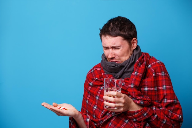 Een in een deken gewikkelde zieke man met tabletten en mok in zijn handen