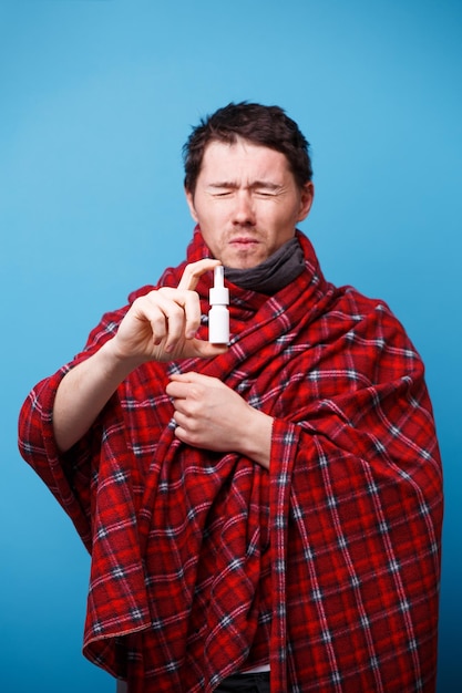 Een in een deken gewikkelde zieke man staat met neusspray in zijn hand