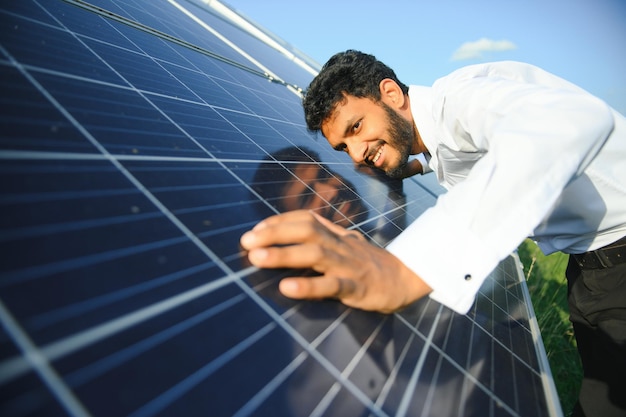Een Indiase mannelijke ingenieur in een groen vest werkt aan een veld met zonnepanelen. Het concept van hernieuwbare energie