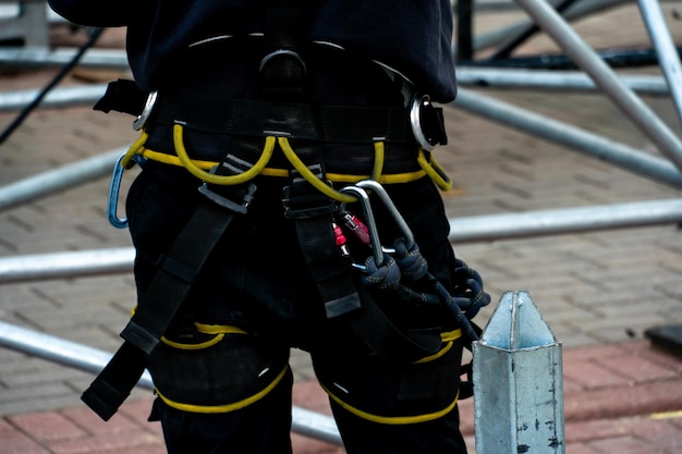 Een industriële klimmer die een helm en een beschermende riem draagt, is op grote hoogte met een touw aan een steun vastgebonden Een specialist assembleert een toneelstructuur uit een modulair systeem van metalen steigers