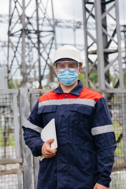 Een ingenieur in het onderstation inspecteert moderne hoogspanningsapparatuur in een masker op het moment van pondemia. Energie. Industrie.