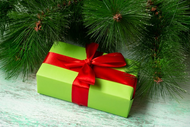 Een ingepakt groen cadeau met een rood lint ligt onder een kerstboom op een houten vloer