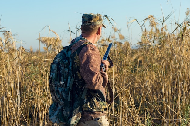 Een jager met een pistool in zijn handen in jachtkleding in het herfstbos op zoek naar een trofee