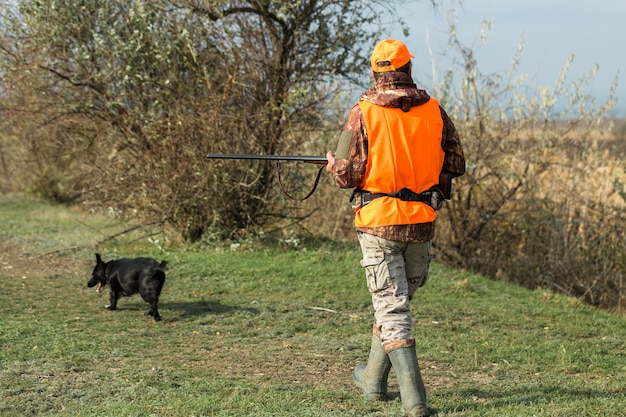 Een jager met een pistool in zijn handen in jachtkleding in het herfstbos op zoek naar een trofee