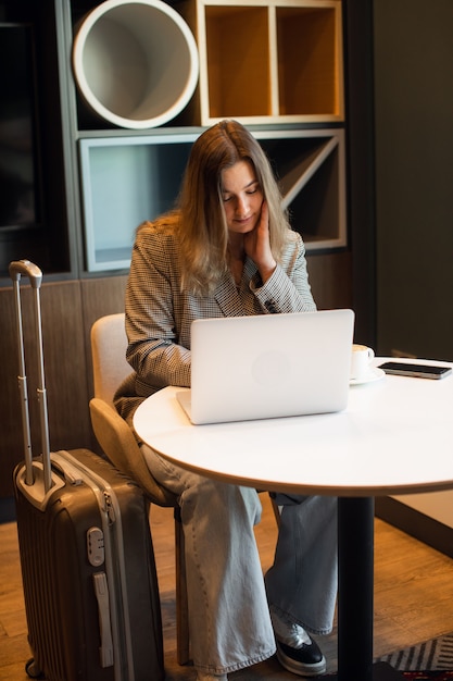 Een jong, aantrekkelijk mollig meisje zit in een café koffie te drinken en werkt op een laptop van hoge kwaliteit foto