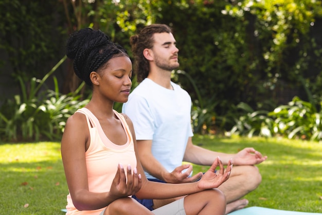 Een jong Afro-Amerikaans echtpaar en een blanke man mediteren in een serene tuin.