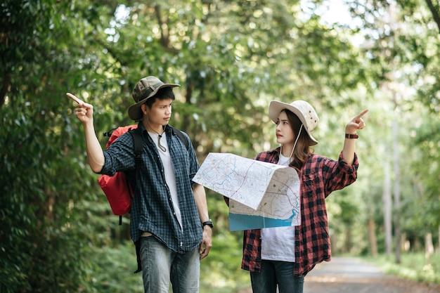Een jong backpackerpaar met een hoed en een papieren kaart maakt ruzie over de richting van het bospad.