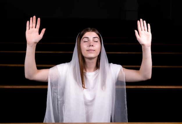 Een jong bescheiden meisje met een zakdoek op haar hoofd zit in de kerk en bidt.