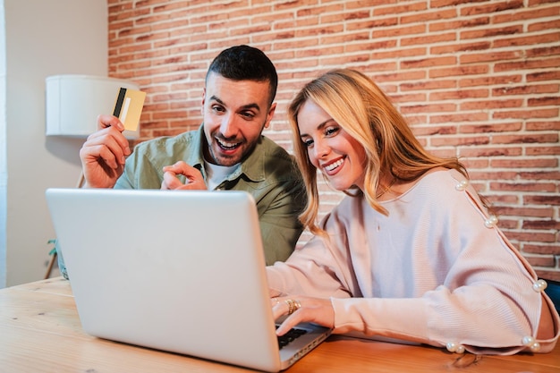 Een jong blank echtpaar gebruikt een laptop om een online bestelling te plaatsen en te betalen met hun krediet