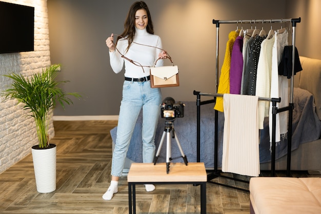 Een jong blogger-meisje met donker haar laat haar kleding en tassen zien aan haar volgers op sociale media om het online te verkopen