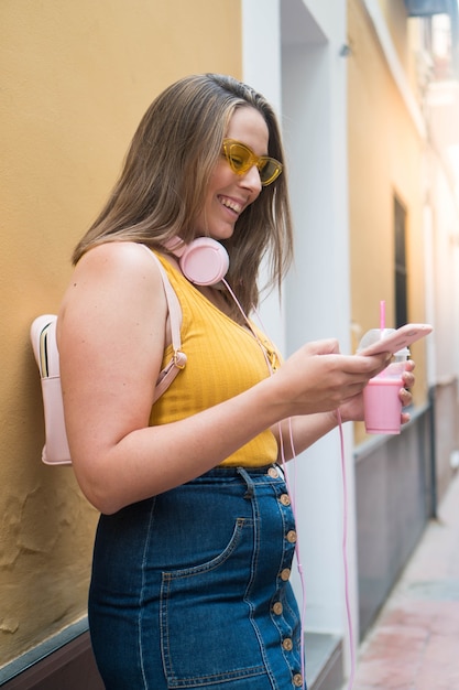 Een jong brunette meisje lacht naar haar telefoon en luistert naar muziek op straat