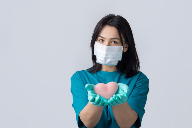 Een jong donkerbruin meisje met een beschermend medisch masker met een roze hart symboliseert het leven Coronavirus